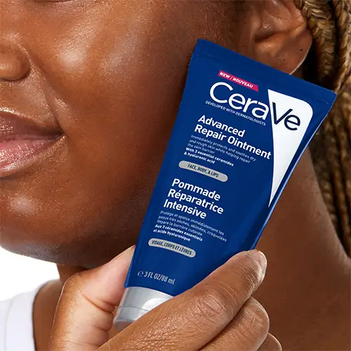 Woman with glowing skin, holding CeraVe Advanced Repair Ointment up to her cheek